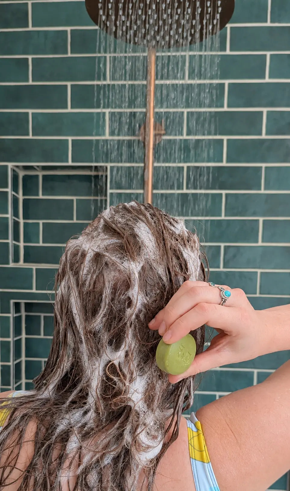 Person in the shower lathering a solid shampoo bar into their scalp