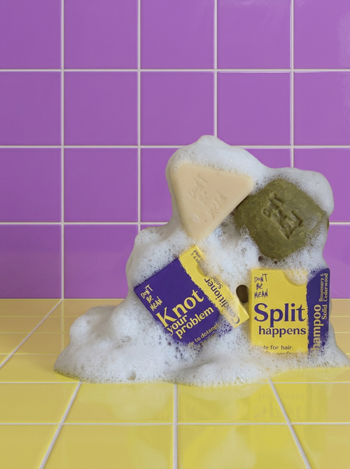 Solid shampoo and conditioner bars with their boxes in a pile of foam on yellow and purple tiles