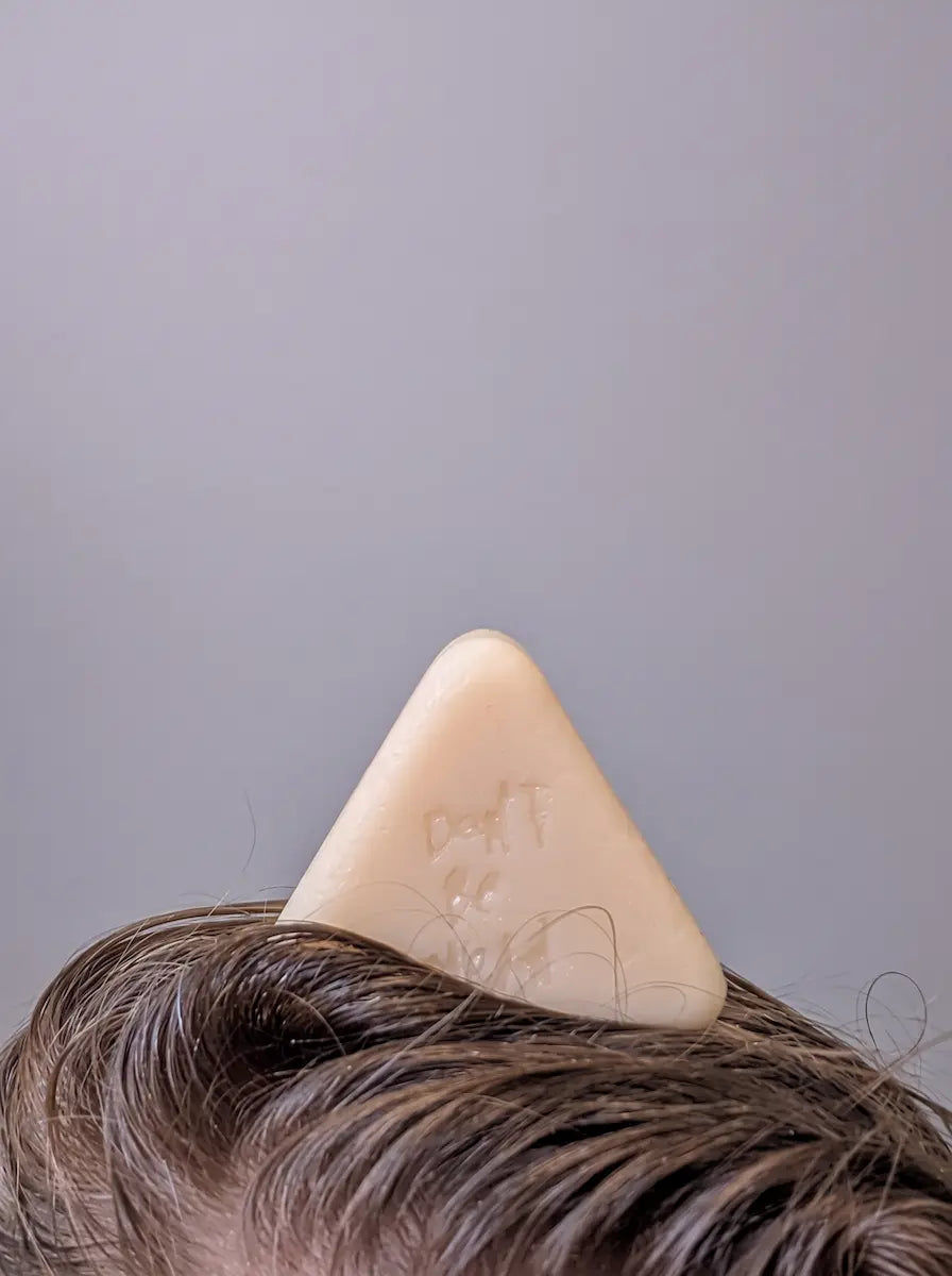 Triangular solid conditioner bar standing on top of brown hair