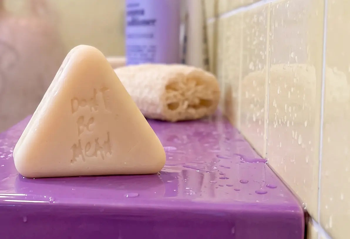 Solid conditioner bar embossed with Don't Be Mean on a purple shower shelf