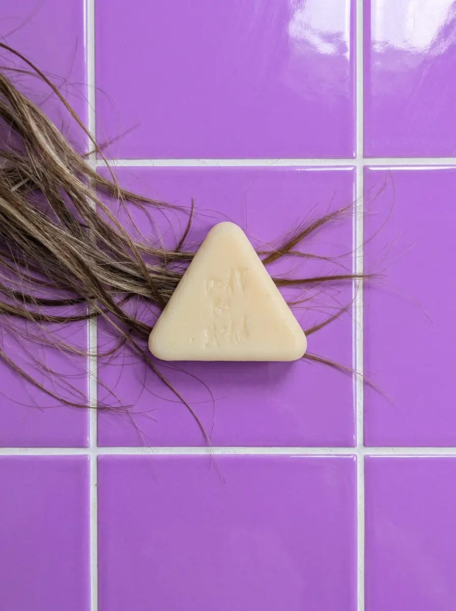 Triangular cream solid conditioner bar on purple tiles with strands of hair