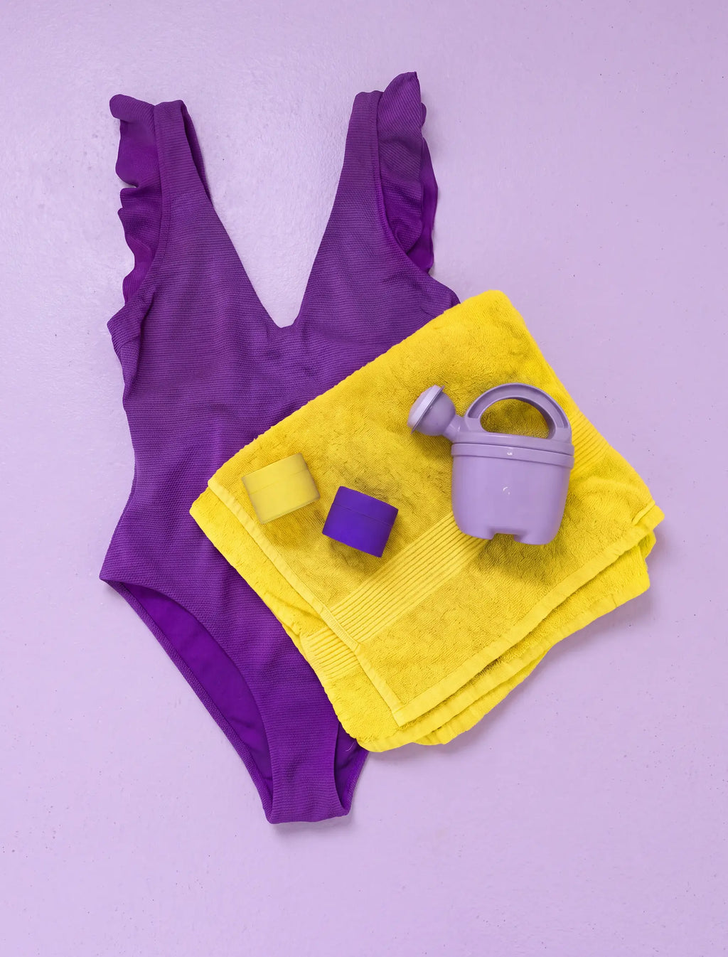 Two Mini Just in Case silicone cases on a yellow towel with a purple swimsuit and toy watering can