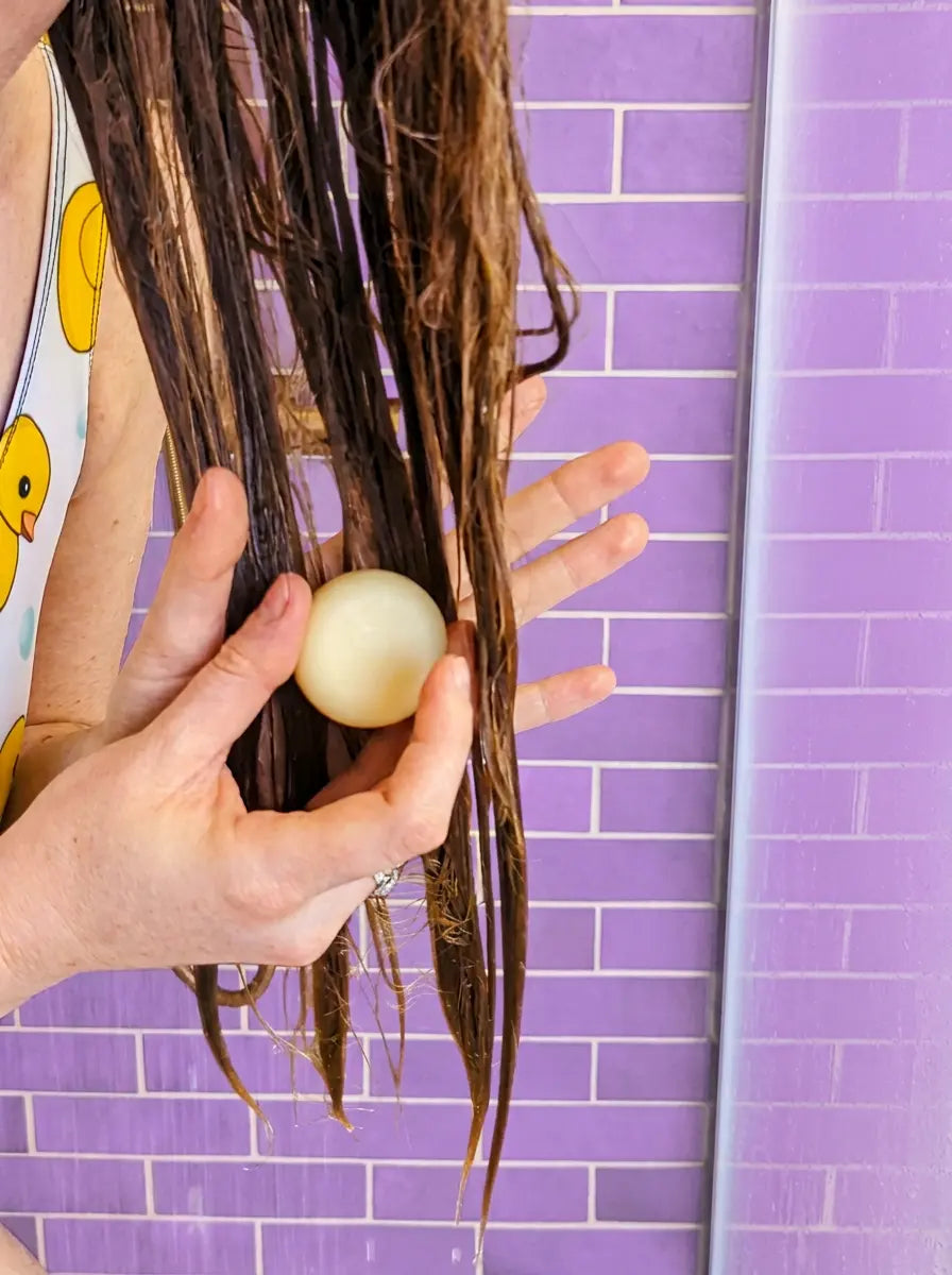 Hand gliding a travel-size conditioner bar down the lengths of wet hair