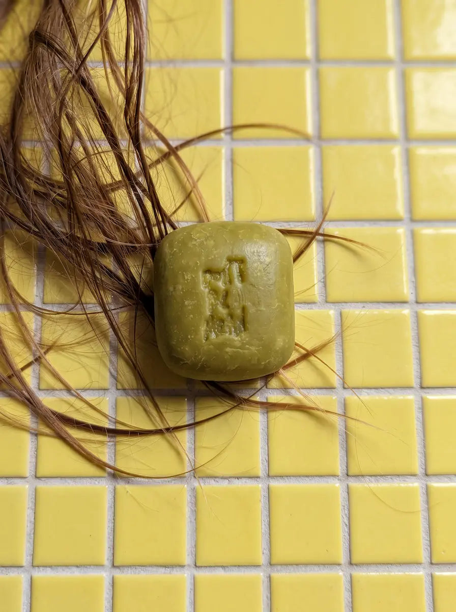 Green solid shampoo bar on yellow tiles with strands of hair