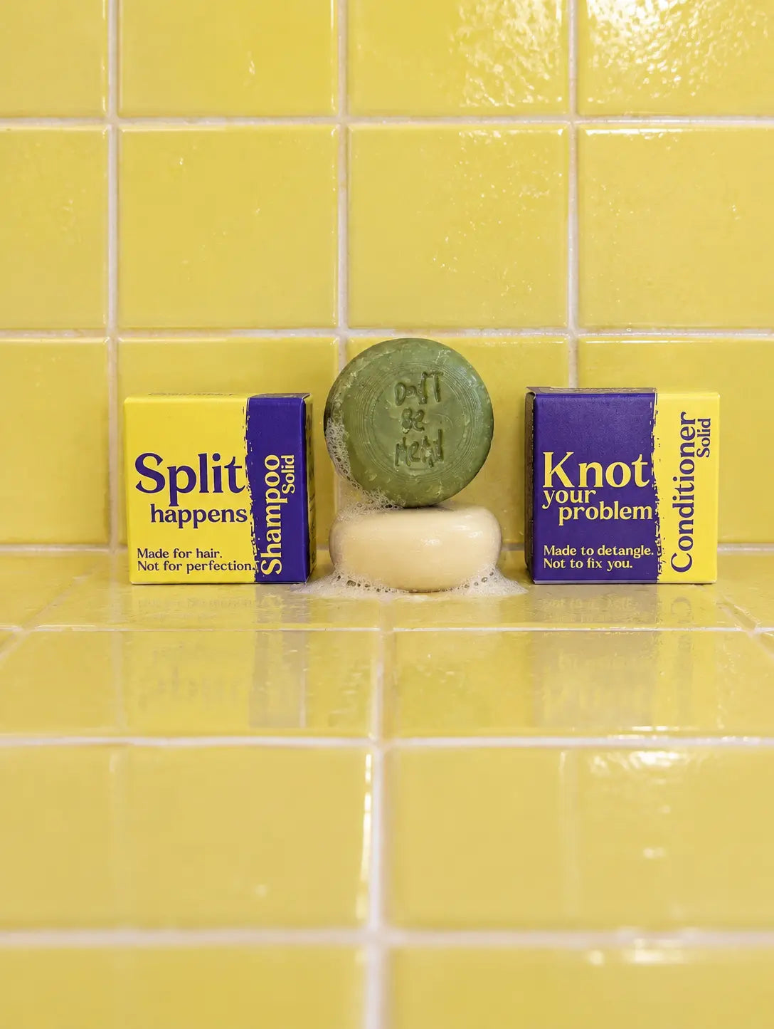Travel-size solid shampoo and conditioner bars stacked between their boxes on yellow tiles