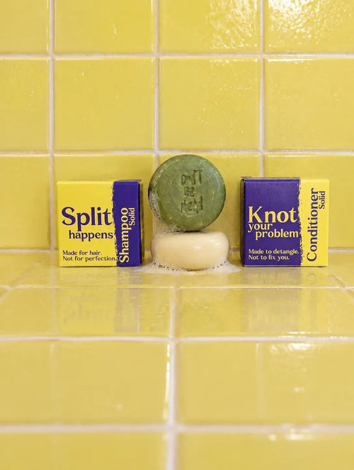 Travel-size solid shampoo and conditioner bars stacked between their boxes on yellow tiles
