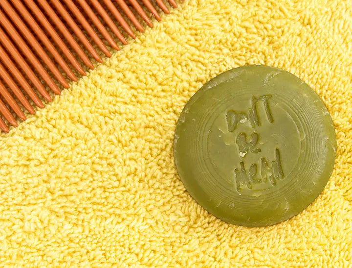 Round green travel-size shampoo bar on a yellow towel next to a wooden comb