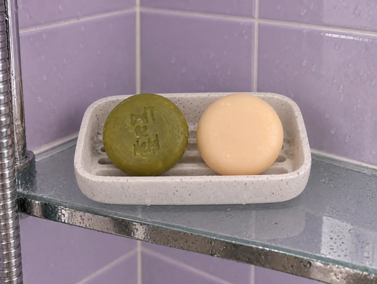 Round travel-size shampoo and conditioner bars in a soap dish on a shower shelf